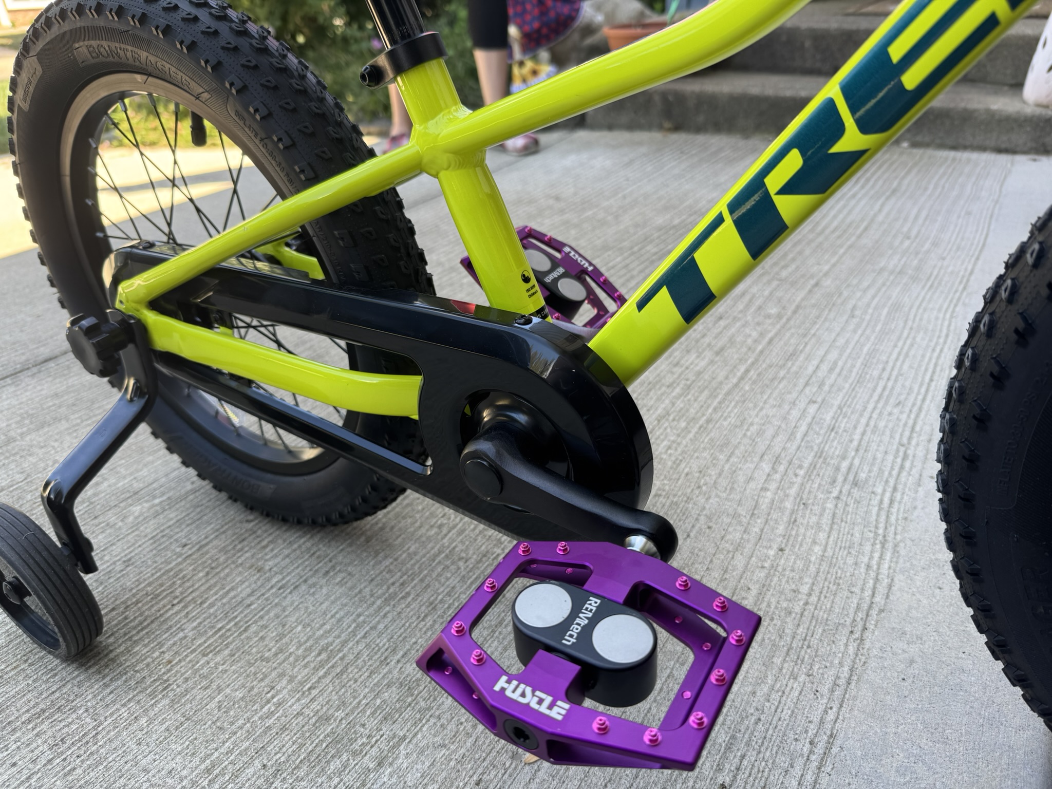 Close up of purple Hustle Bike Labs magnetic pedals mounted on a child's bike with training wheels
