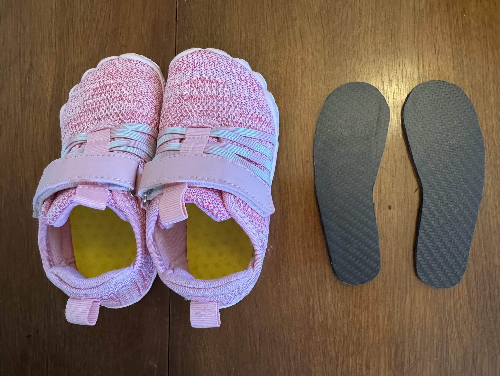 Pair of pink kids sneakers next to two gray magnetic shoe inserts on a wood table