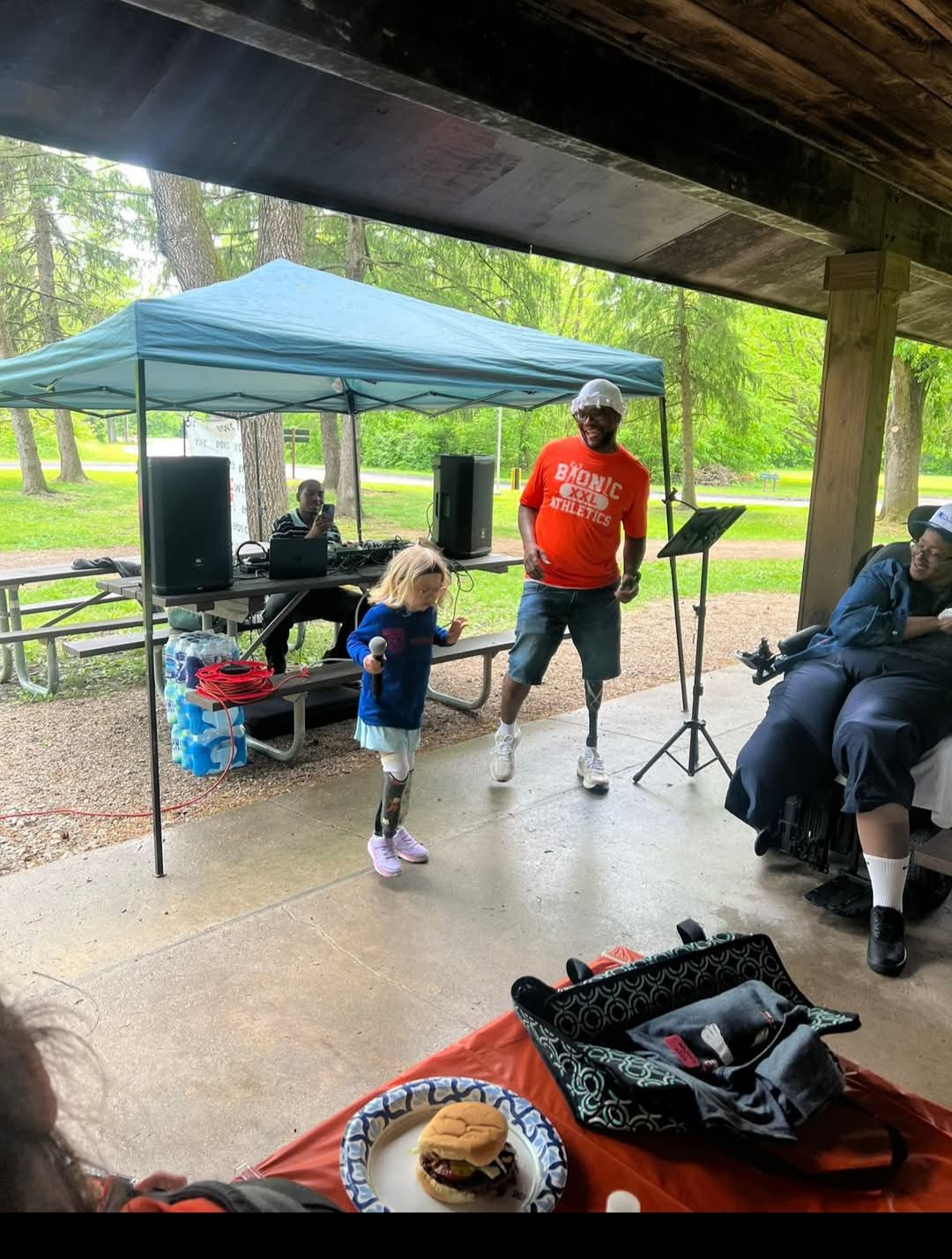 Gwen holding a microphone at the Byonic Limb Loss Awareness Picnic, standing next to an adult amputee in a Byonic shirt