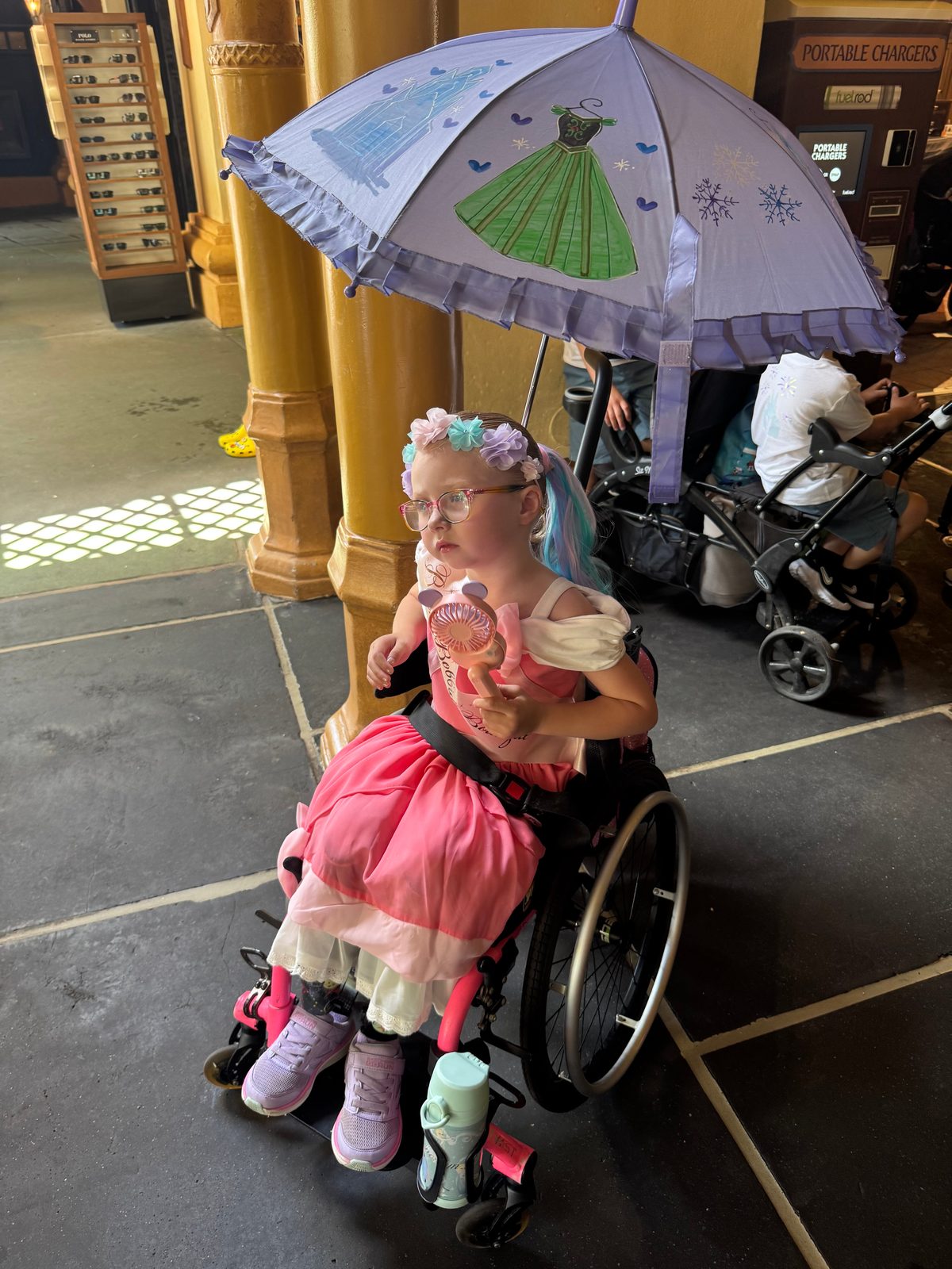 Gwen using her pediatric wheelchair with an umbrella attached for shade at Disney World