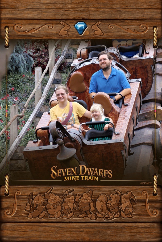 Gwen sitting between her parents on the Seven Dwarfs Mine Train roller coaster at Disney World. All three are smiling mid-ride.