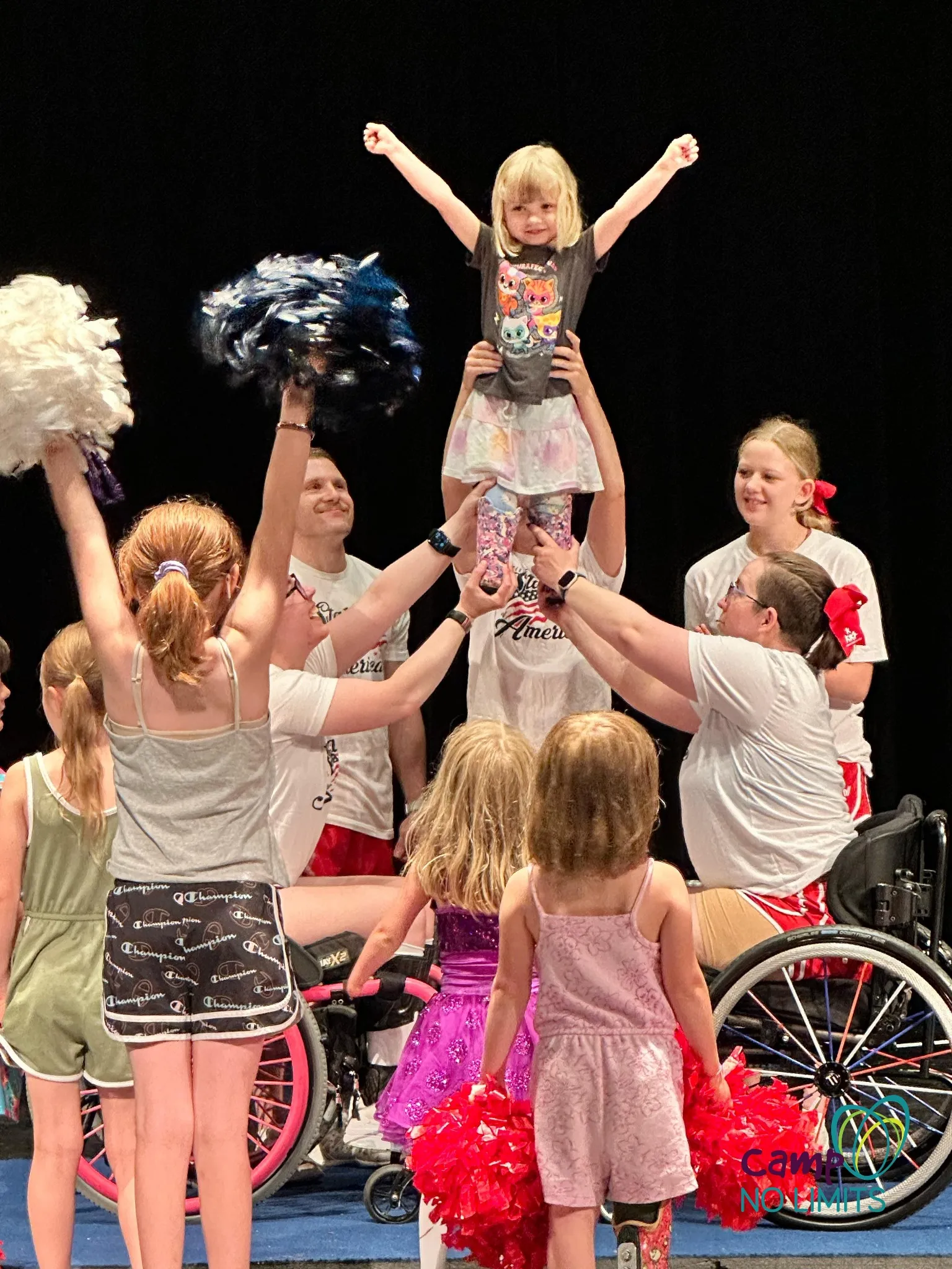 Gwen being lifted in a cheer stunt at a ParaCheer event with kids and coaches, some using wheelchairs, cheering her on