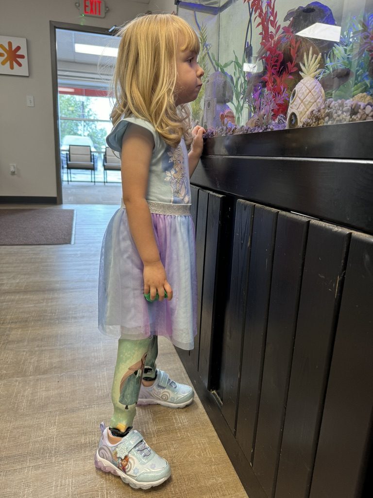 Gwen standing by an aquarium wearing her third set of prosthetics with Frozen designs